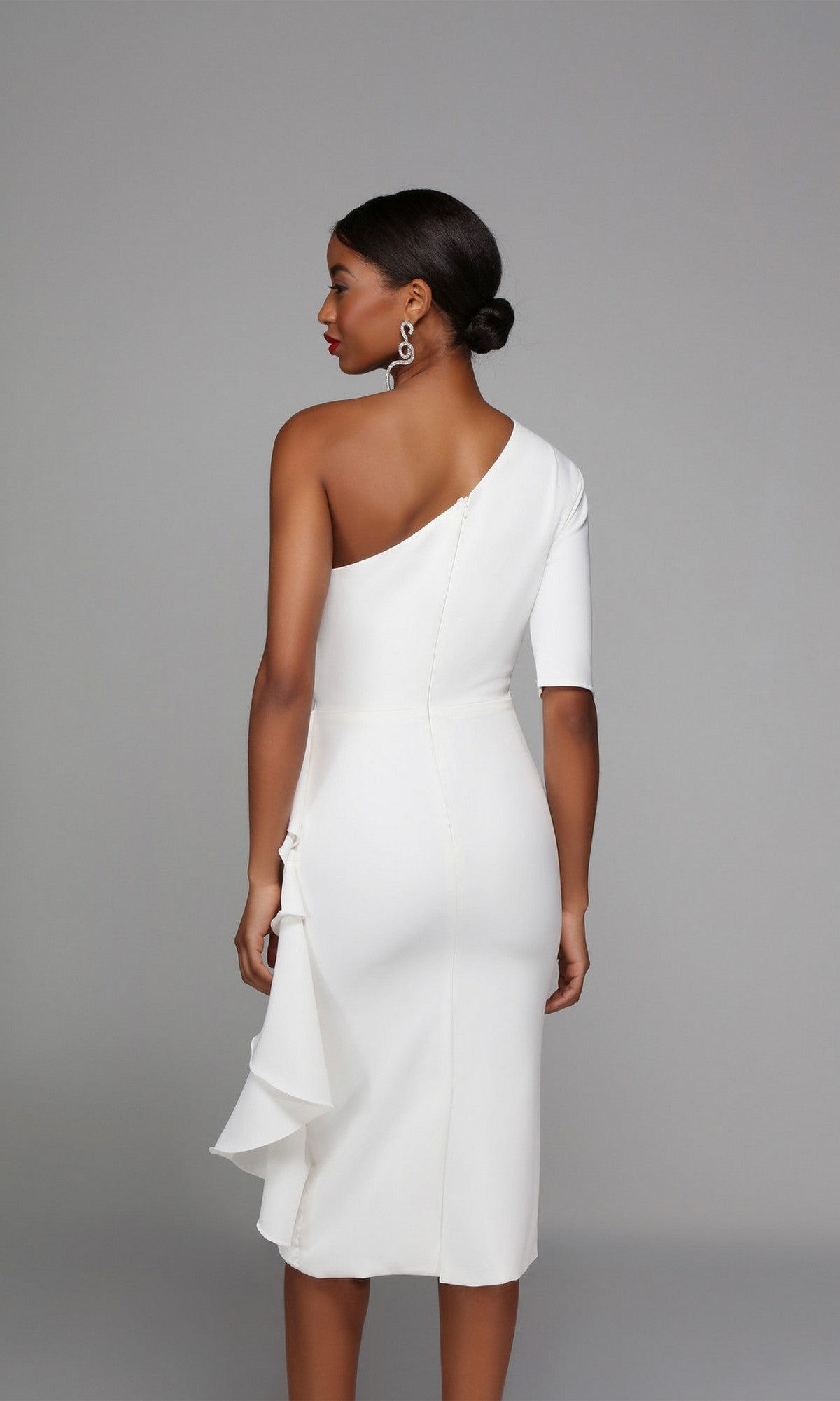A woman models the Alyce 70006 knee-length semi-formal dress, featuring a fitted white one-shoulder design with an asymmetrical sleeve and ruffle detail, set against a plain gray background.